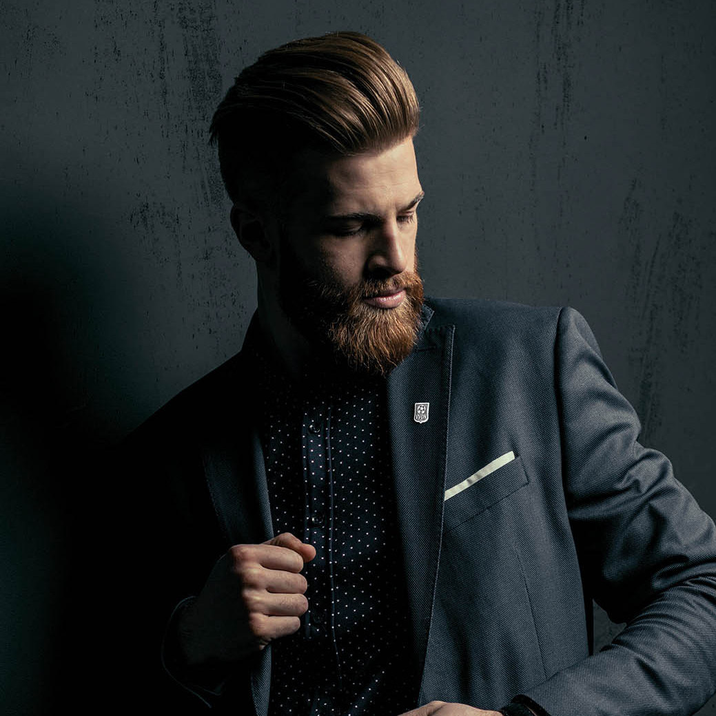 Stylish handsome bearded man in trendy suit posing on black